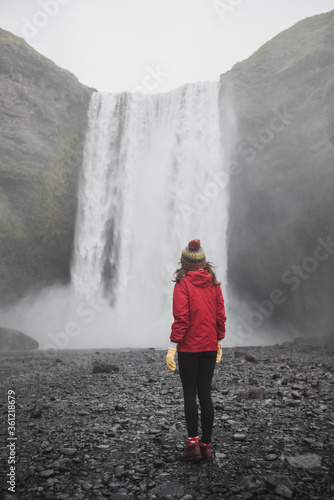 Iceland landscape photo of brave girl who proudly standing with his arms raised in front of water wall of mighty waterfall.