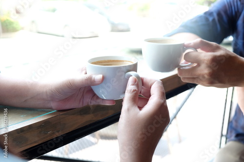 Two younger drinking coffee together, Couple lover having a break drinking coffee in bar ,Close-up shot of hand holding cup of coffee 