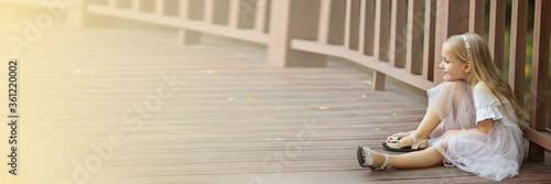 Happy stylish little girl with blonde hair sitting alone on the wooden bridge in the park. The end of COVID-19 Pandemic crisis and lockdown. happiness and hope, stop virus spreading.