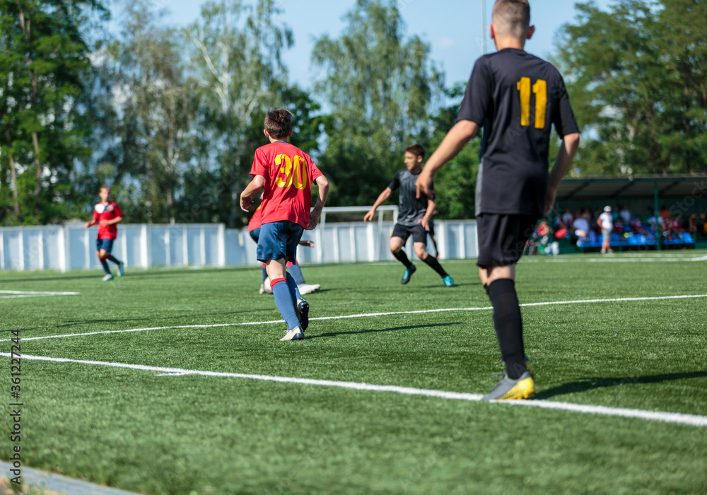 Boys in red and black sportswear plays football on field, dribbles ball. Young soccer players with ball on green grass. Training, football, active lifestyle for kids Boys in red and black sportswear plays football on field, dribbles ball. Young soccer players with ball on green grass. Training, football, active lifestyle for kids
