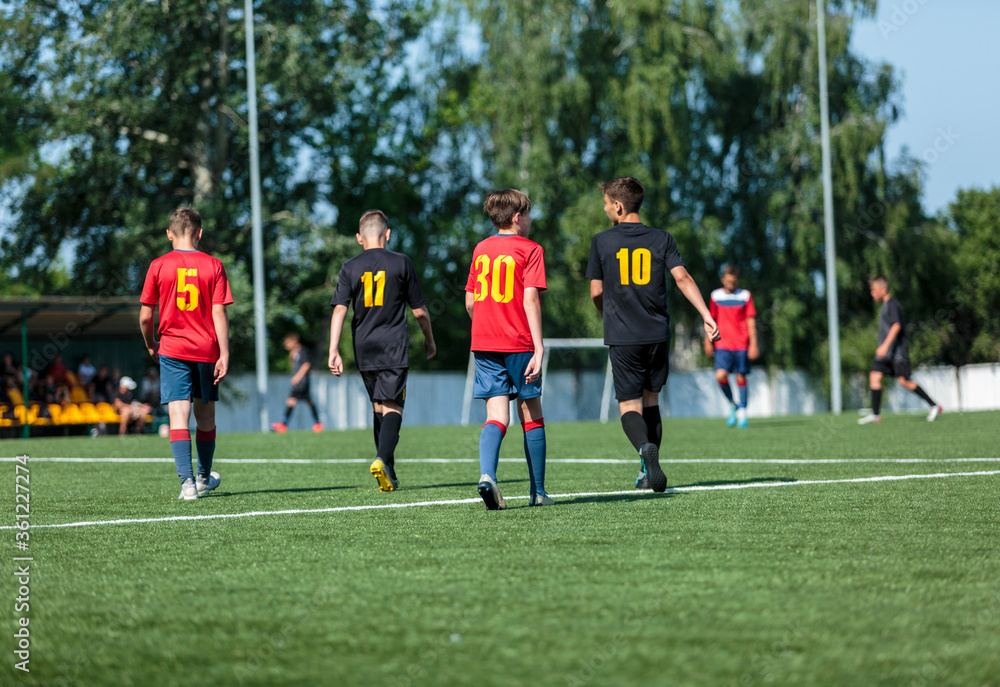 Boys in red and black sportswear plays football on field, dribbles ball. Young soccer players with ball on green grass. Training, football, active lifestyle for kids Boys in red and black sportswear plays football on field, dribbles ball. Young soccer players with ball on green grass. Training, football, active lifestyle for kids