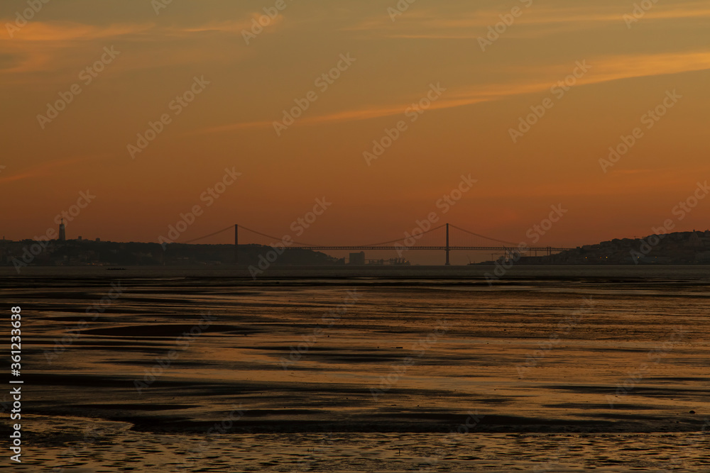 Low light image taken at sunset on the banks of Tagus River that lies between Almada and Lisbon. It features silhouettes of both cities, the 25 de abril suspension bridge and Christ the king monument.