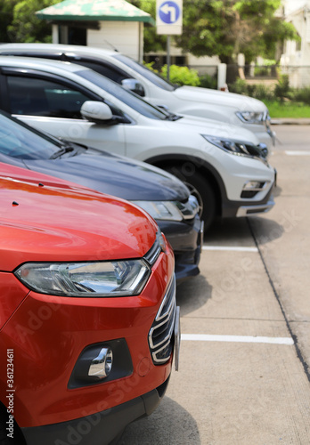 Closeup of front side of red car with other cars parking in outdoor parking area in bright sunny day. Vertical view.