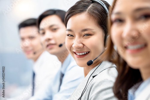 Smiling cheerful Asian woman working in call center office with team as customer service operators