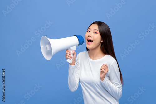 Cheerful cute Asian woman talking on magaphone isolated on blue background photo