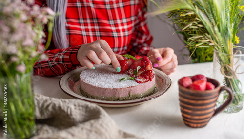 Woman is decorating a delicious strawberry mousse cake with berries. Concept of tasty and healthy summer desserts