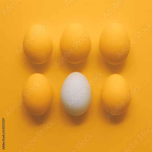 Eggs on yellow background. One white egg and five yellow eggs.