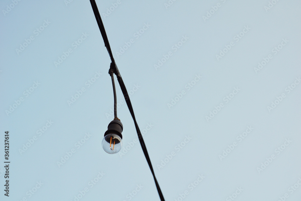 Light bulb hanging on a electricity wire with blue clear sky background. Light bulb hanging on a electricity wire with blue clear sky background.