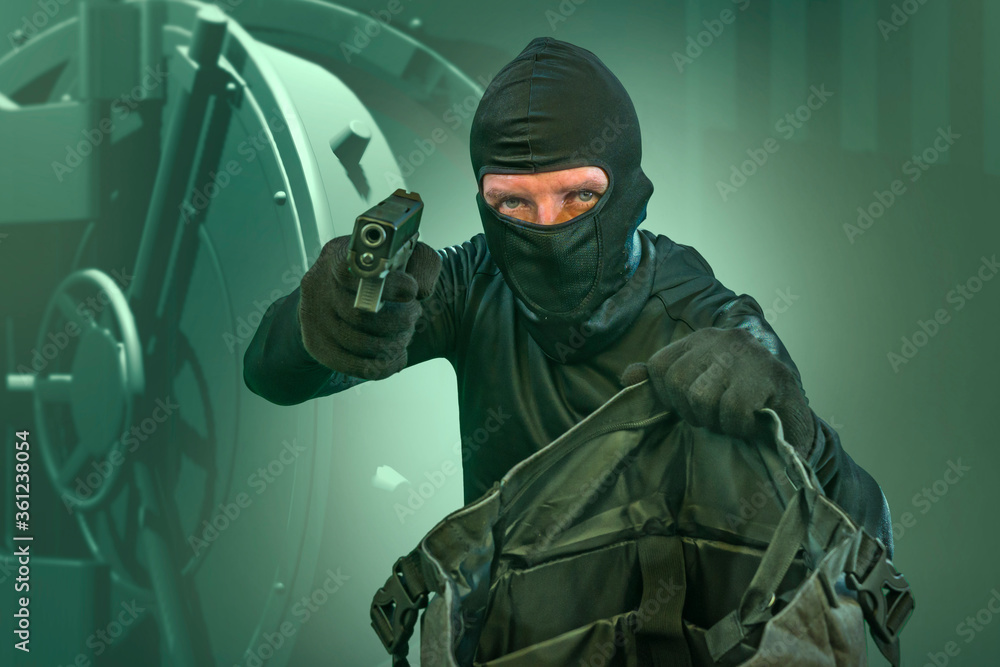 heist and robbery - Hollywood style portrait of man in balaclava mask holding gun in front of security metal vault door in bank or casino heist concept stealing money heist and robbery - Hollywood style portrait of man in balaclava mask holding gun in front of security metal vault door in bank or casino heist concept stealing money