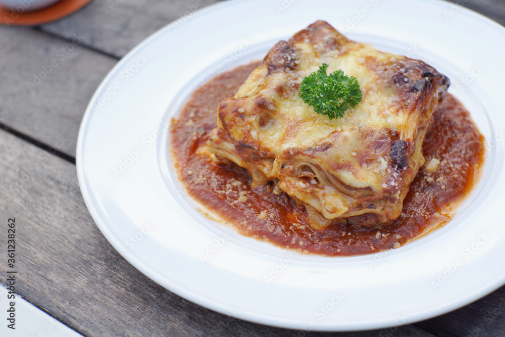 Close up of meat lasagna on a white plate with wooden table background.