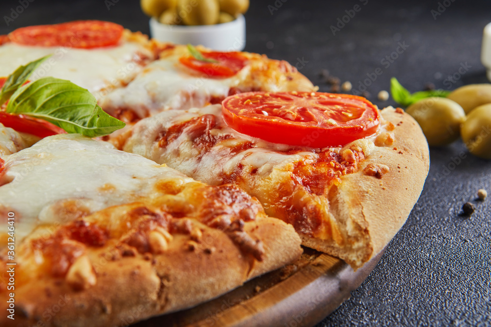 Italian pizza and ingredients for cooking on a black concrete background. Tomatoes, olives, basil and spices. Sliced triangle of pizza. Italian pizza and ingredients for cooking on a black concrete background. Tomatoes, olives, basil and spices. Sliced triangle of pizza.