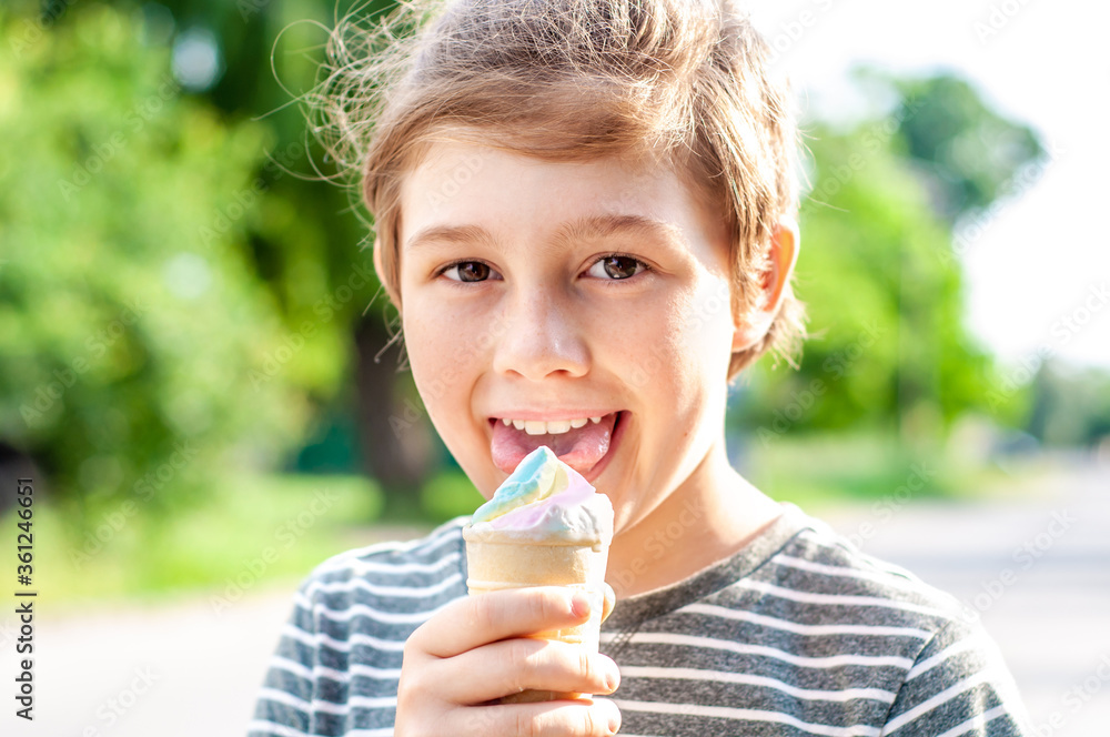Fashionable boy eating multicolored ice cream in a waffle cone. Cool in the summer heat. Sweet snack. Hot Summer. Emotional child licks ice cream Fashionable boy eating multicolored ice cream in a waffle cone. Cool in the summer heat. Sweet snack. Hot Summer. Emotional child licks ice cream