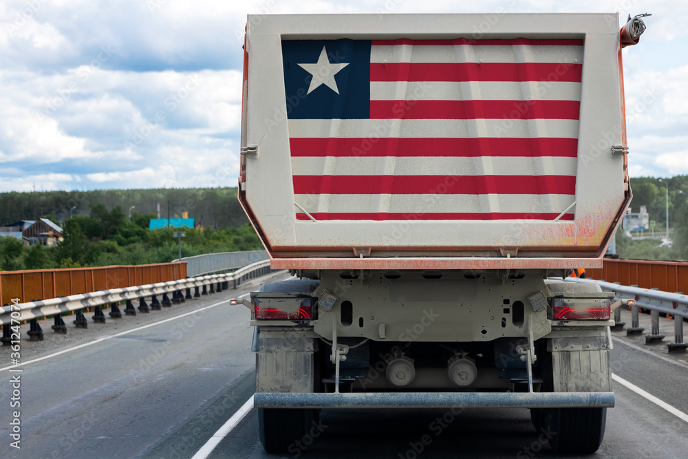 Big dirty truck with the national flag of Liberia moving on the highway, against the background of the village and forest landscape. Concept of export-import,transportation, national delivery of goods