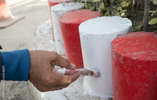 The hand of a man holding the handle to paint the curb White and red. Parking is prohibited in accordance with traffic regulations.