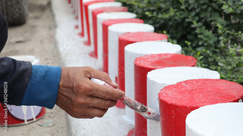 The hand of a man holding the handle to paint the curb White and red. Parking is prohibited in accordance with traffic regulations.