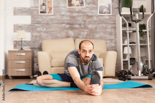 Healthy man doing mobily exercise on yoga mat at home during global pandemic. photo