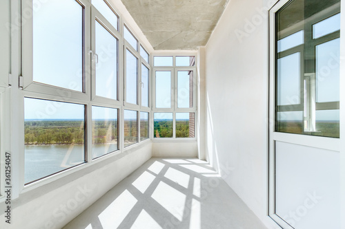 A sunny balcony with the panoramic windows in a new residential building on the high floor. A light loggia with white plastered walls without decoration