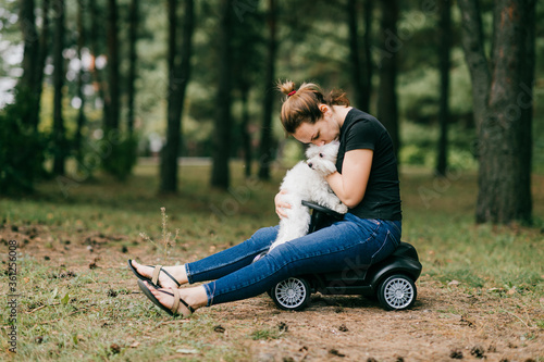 Beautiful caucasian woman with dark hair sits on the little toy car and plays with her little pet dog in the park