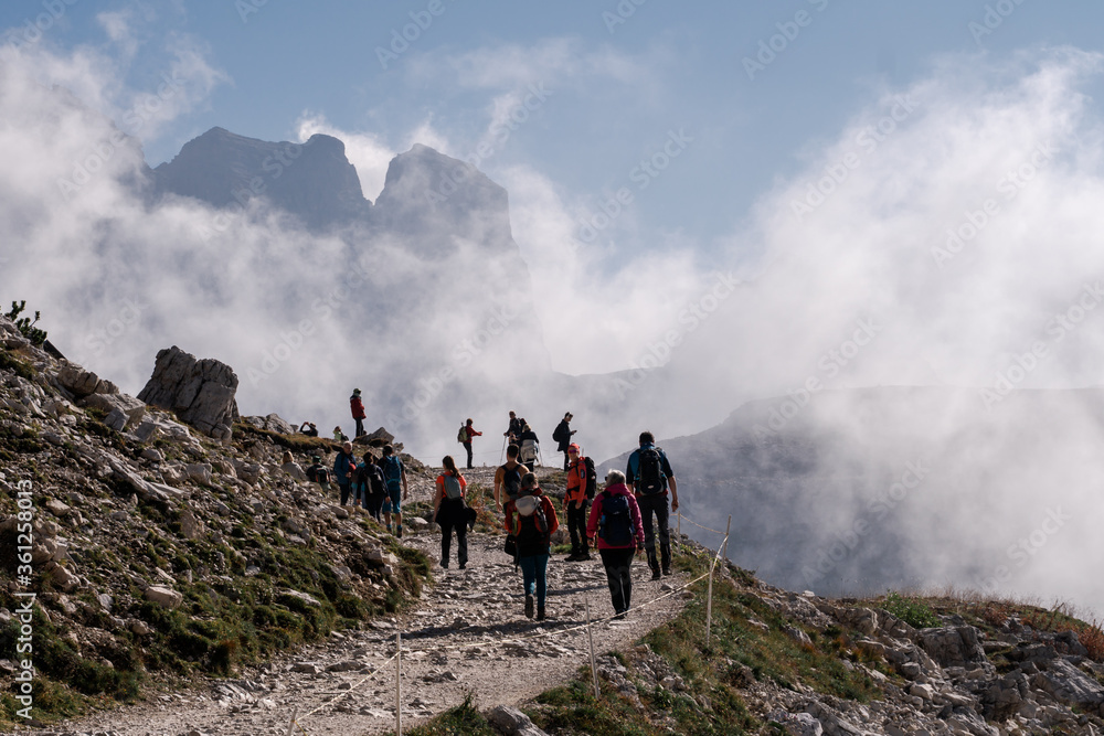 Tre Cime di Lavaredo. Italy - 09.29.2019. Dolomites Alps. Group of tourists hike in mountains on background of blue sky &  thick clouds in sunny summer day