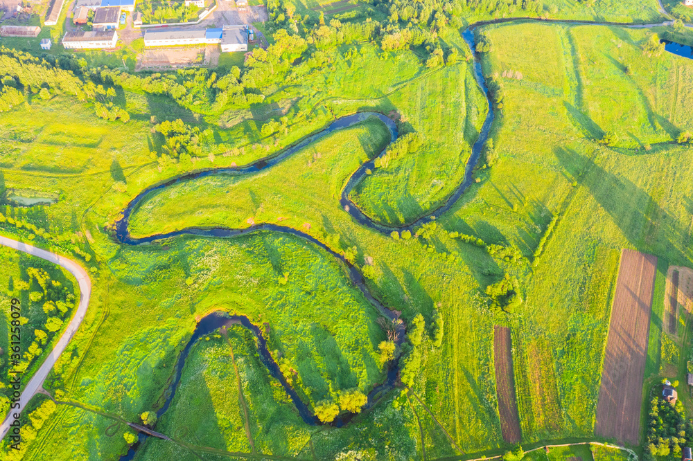Obraz premium Top aerial view of the natural rural landscape valley of a meandering river among green fields and forests.