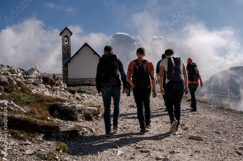 Tre Cime di Lavaredo. Italy - 09.29.2019. Dolomites Alps. Group of tourists hike in mountains to alpine chapel on background of blue sky & thick clouds in sunny summer day