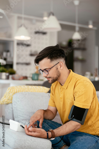 Young man measuring blood pressure. Sick young man in living room. 