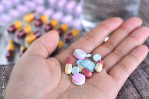 Pills on woman' s hand with medicine panels and glass of water background