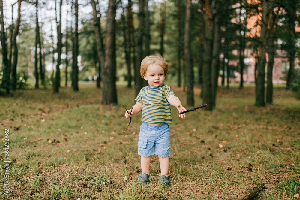 Little beautiful caucasian boy with short fair hair in blue shirt and blue shorts spend a lot of time in the summer park Little beautiful caucasian boy with short fair hair in blue shirt and blue shorts spend a lot of time in the summer park