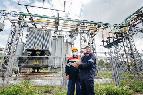 Engineers electrical substations conduct a survey of modern high-voltage equipment in the mask at the time of pandemia. Energy. Industry