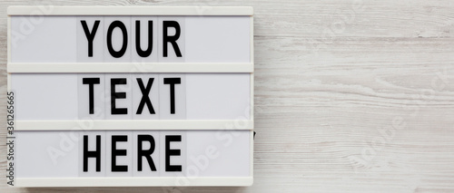 'Your text here' words on a lightbox on a white wooden background, top view. Flat lay, overhead. Copy space.