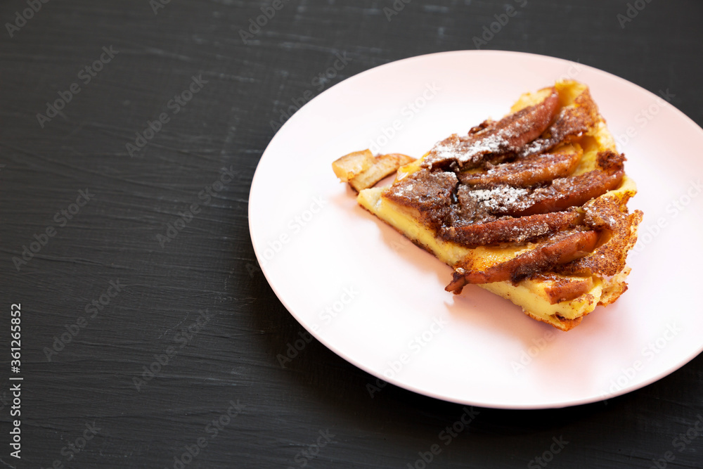 Homemade Apple Dutch Pannekoek Pancake on a pink plate on a black surface, side view. Copy space. Homemade Apple Dutch Pannekoek Pancake on a pink plate on a black surface, side view. Copy space.