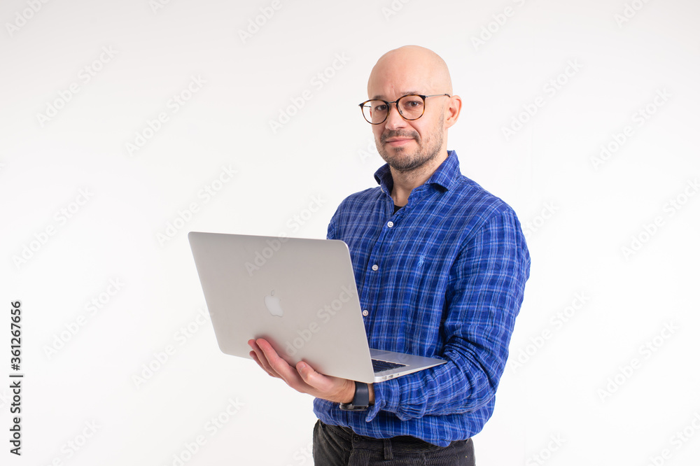 Handsome caucasian man without hair in blue shirt, black trousers and blue socks do freelance with laptop isolated on white background Handsome caucasian man without hair in blue shirt, black trousers and blue socks do freelance with laptop isolated on white background