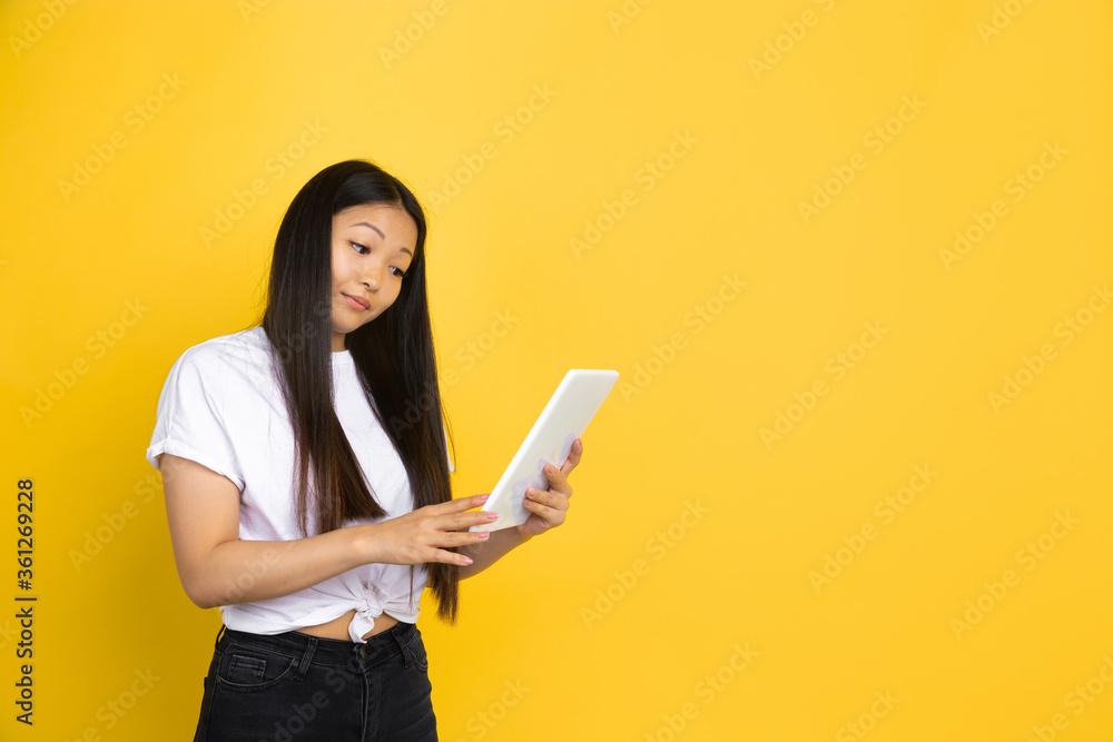 Using tablet, ordering. Portrait of young asian woman on yellow studio background. Stylish, trendy. Beautiful brunette model. Human emotions, facial expression, sales, ad, shopping concept. Copyspace. Using tablet, ordering. Portrait of young asian woman on yellow studio background. Stylish, trendy. Beautiful brunette model. Human emotions, facial expression, sales, ad, shopping concept. Copyspace.