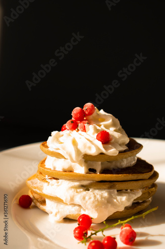 Banana pancake with red currant berries and whipped cream on a white plate, on a black background