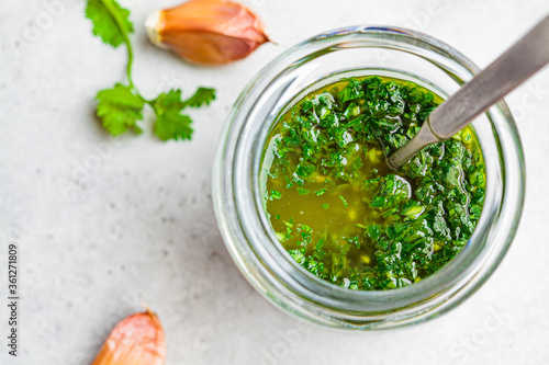 Fresh traditional chimichurri sauce for barbecue meat in glass jar, light background, top view. photo