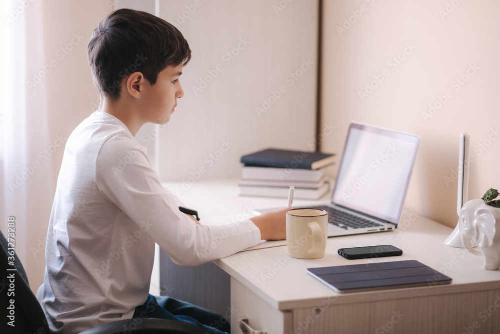 Schoolboy study at desk in his room. Boy use laptop for lessons. Drink tea. Books and tablet on the table. Study home during qurantine Schoolboy study at desk in his room. Boy use laptop for lessons. Drink tea. Books and tablet on the table. Study home during qurantine