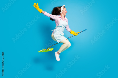 Full length body size profile side view of her she nice attractive funky childish comic maid jumping riding broom like horse isolated on bright vivid shine vibrant blue color background photo