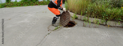 A worker in uniform lifts the sewer header cover.