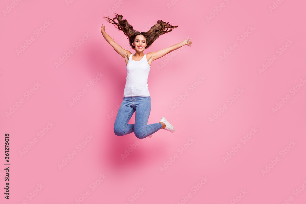 Full size photo of attractive funky lady jumping high up spread hands good mood cheerful sunny day weekend wear white casual singlet jeans shoes isolated pink color background