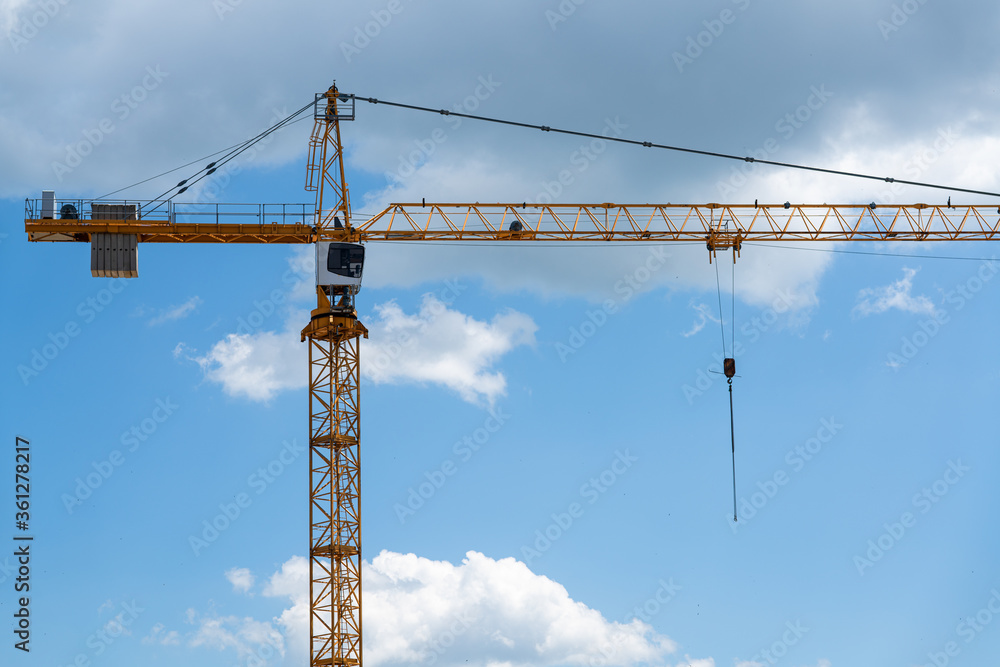 Construction of a building with a construction crane against the blue and cloudy sky.