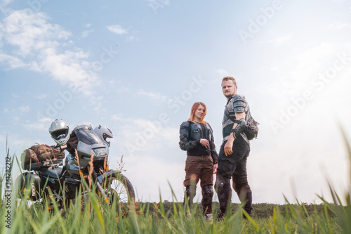 A pair of motorcyclists, man and woman. Loving couple of tourists. Relationship and adventure concept. A motorcycle with luggage, bags and a tent. Side bags. Active lifestyle. Soft light