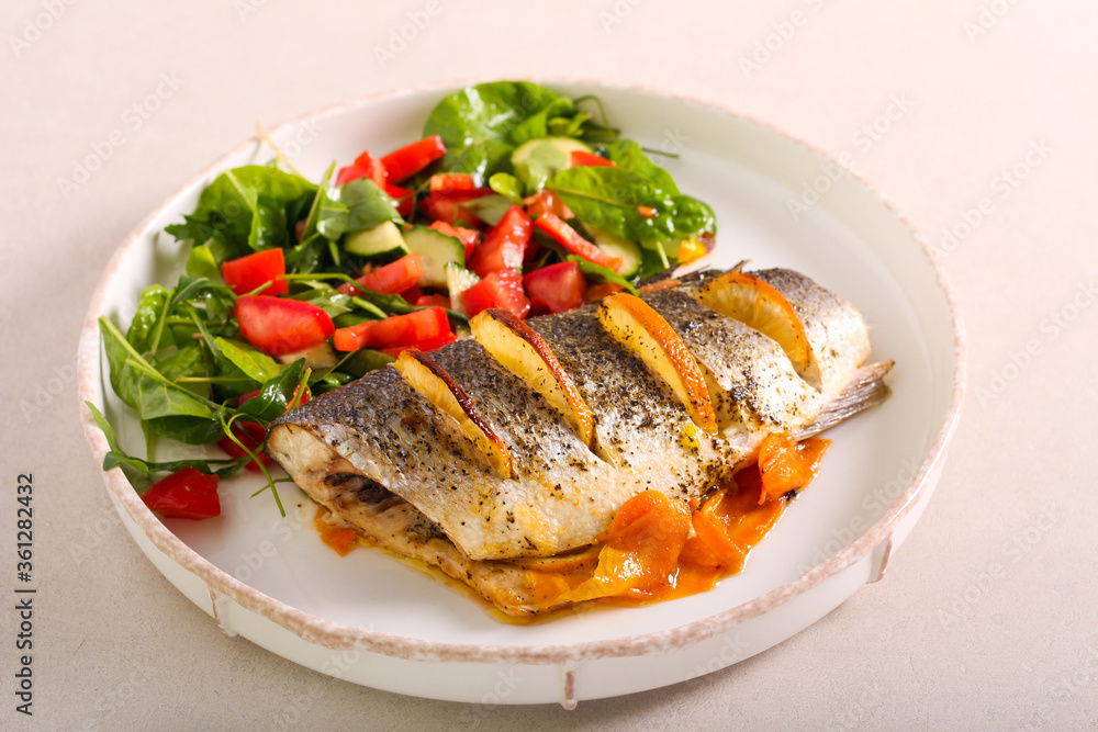 Orange sea bass fish baked on carrot, served with salad Orange sea bass fish baked on carrot, served with salad