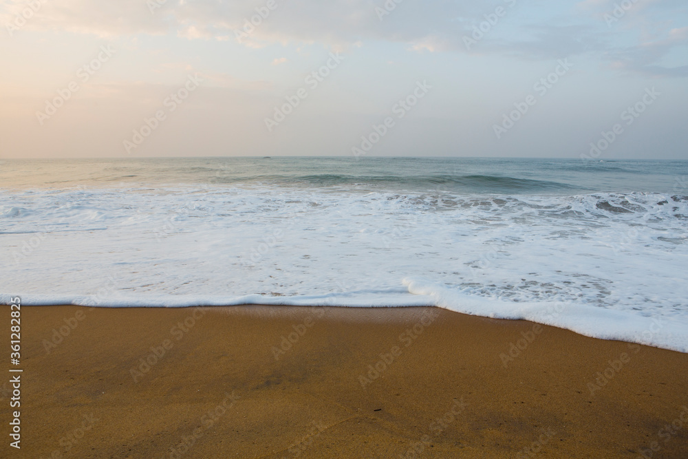 Beautiful seascape shot of the Indian ocean at sunrise with orange sand, a low tide with big white foamy waves and a blue orange sky on the horizon. Pitiwella beach, Sri Lanka