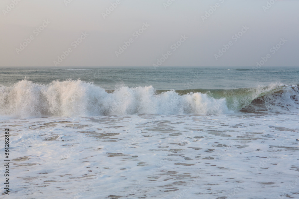 natural copy space shot of a wave crushing on the smooth yellow sand beach surface, forming white foam, with the blue sky on the horizon. Early morning sunrise at Pitiwella beach, Sri Lanka