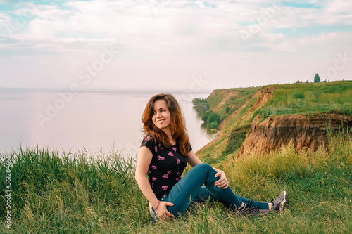 A young girl with long hair sits on the edge of a cliff overlooking the sea, a concept for traveling