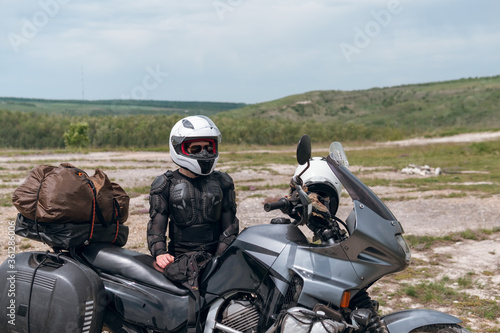 Girl motorcyclist in a helmet. Dressed in a jacket with a turtle, body armor, knee pads. Traveling is an extreme hobby. Safety and body protection. Bike with bags.