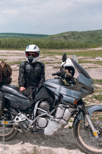 Girl motorcyclist in a helmet. Dressed in a jacket with a turtle  body armor  knee pads. Traveling is an extreme hobby. Safety and body protection. Bike with bags. vertical photo