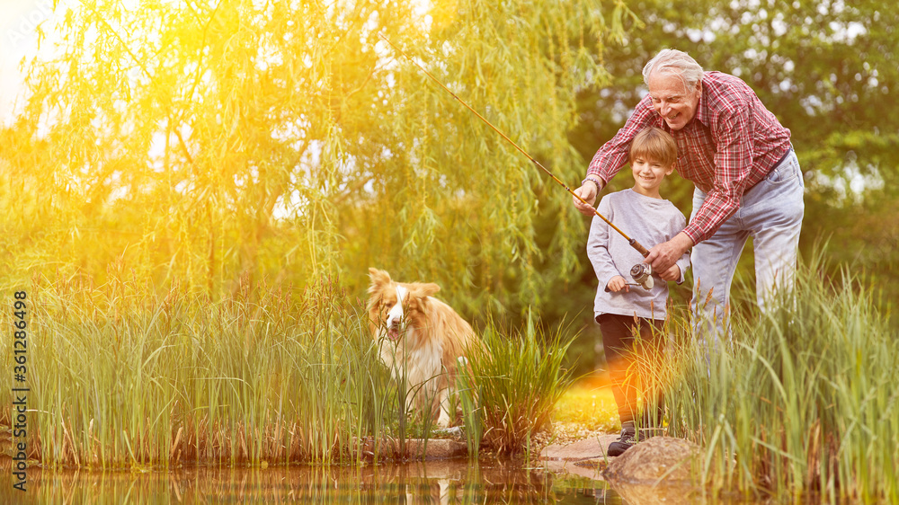 Fototapeta Child fishing with grandpa and dog by the lake in summer