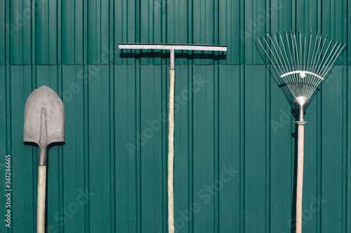 Three gardening working tools standing in yard against shed. Shovel, rake. Farming, working in the garden concept