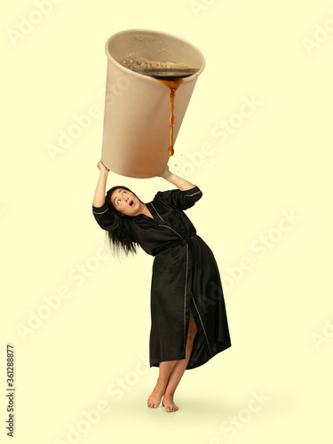 Gas up yourself, filling up with coffee to wake up. Creative artwork. Housewife in black wear holding huge cup with pouring coffee. Looks bored and tired, needs cistern of aroma drink to feel energy. photo